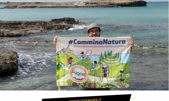 Eco-Passeggiata nel Parco Litorale di Ugento. Man holding #CamminaNatura banner by the sea. Tourism in Ugento.