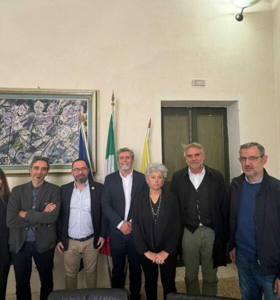Group of people posing for a photo in front of flags and artwork. News event.