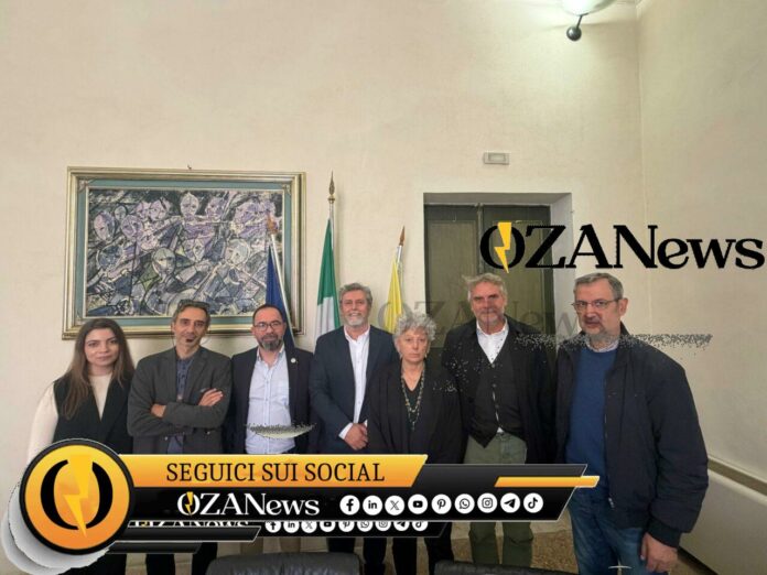 Salento-Libano, con la cooperazione che nutre la pace. A Palazzo Adorno la delegazione del progetto “Caseificio inclusivo in Libano” Group of people posing for a photo in front of flags and artwork. News event.