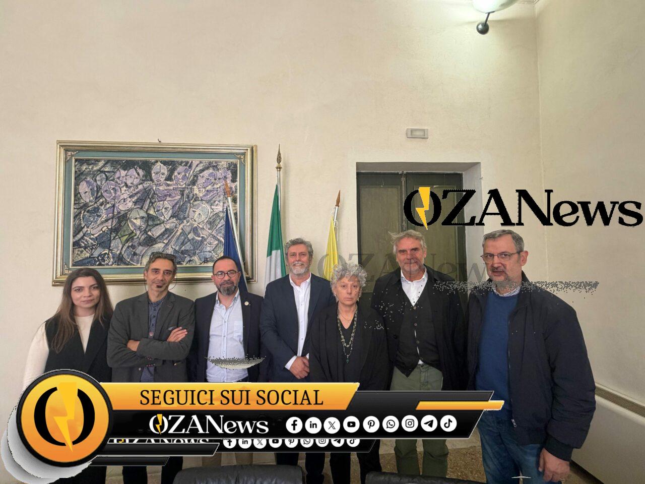 Salento-Libano, con la cooperazione che nutre la pace. A Palazzo Adorno la delegazione del progetto “Caseificio inclusivo in Libano” Group of people posing for a photo in front of flags and artwork. News event.