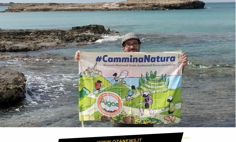 Eco-Passeggiata nel Parco Litorale di Ugento. Man holding #CamminaNatura banner by the sea. Tourism in Ugento.