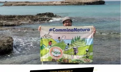 Eco-Passeggiata nel Parco Litorale di Ugento. Man holding #CamminaNatura banner by the sea. Tourism in Ugento.
