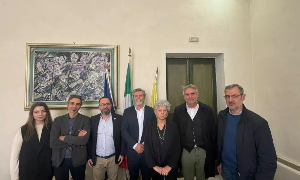 Group of people posing for a photo in front of flags and artwork. News event.