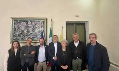 Group of people posing for a photo in front of flags and artwork. News event.