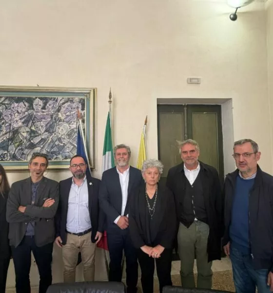 Group of people posing for a photo in front of flags and artwork. News event.